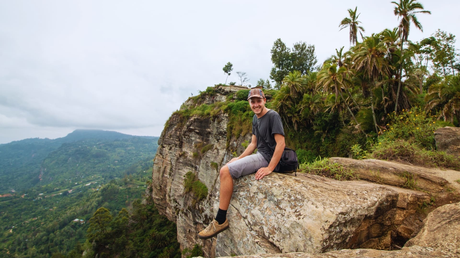 Reiziger zit op een rotsrand met uitzicht over de groene heuvels van Taita Hills in Kenia