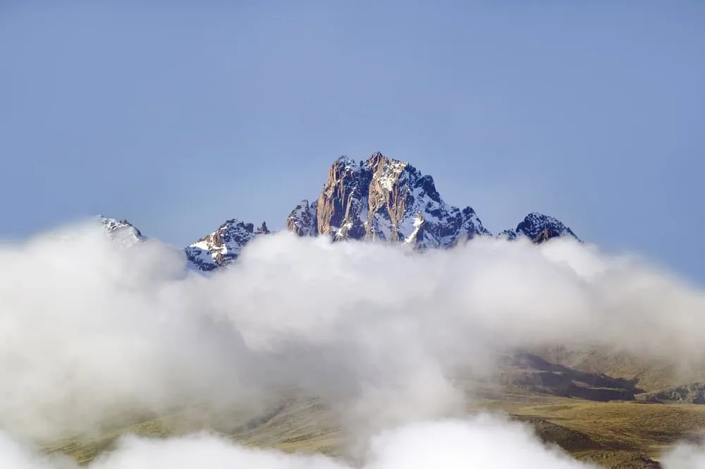 Besneeuwde pieken van Mount Kenya steken boven de wolken uit tegen een heldere blauwe lucht