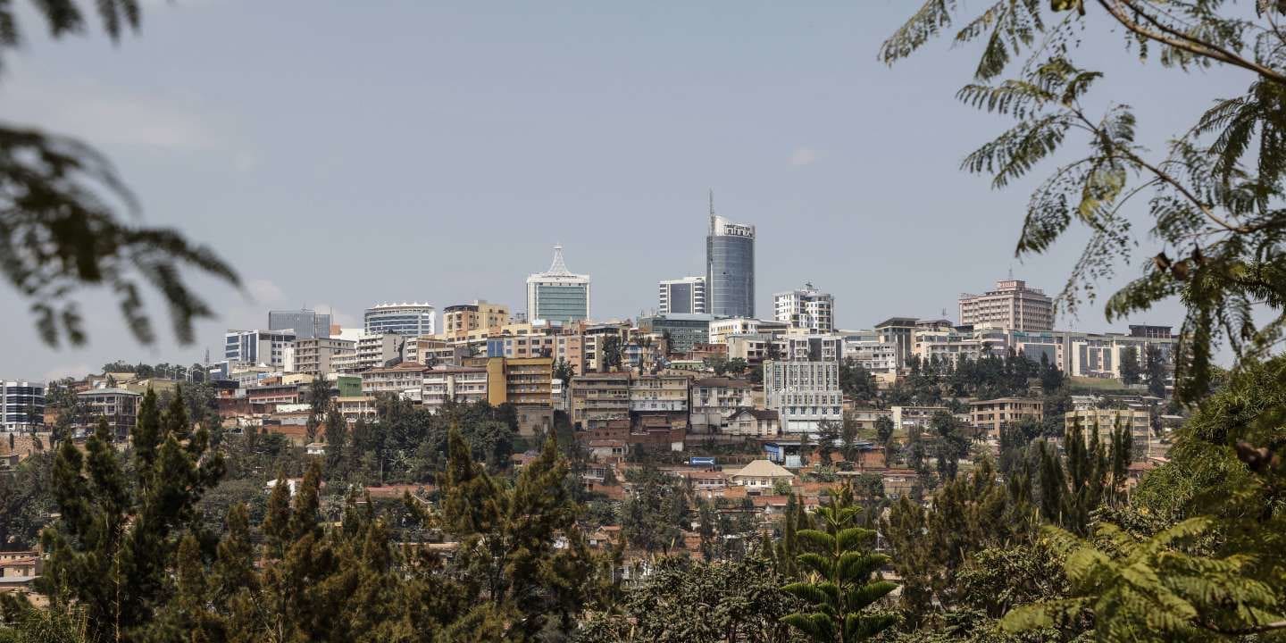 A cityscape of Kigali, Rwanda, in Africa, showcases modern buildings and skyscrapers rising above lush green trees beneath a clear blue sky.