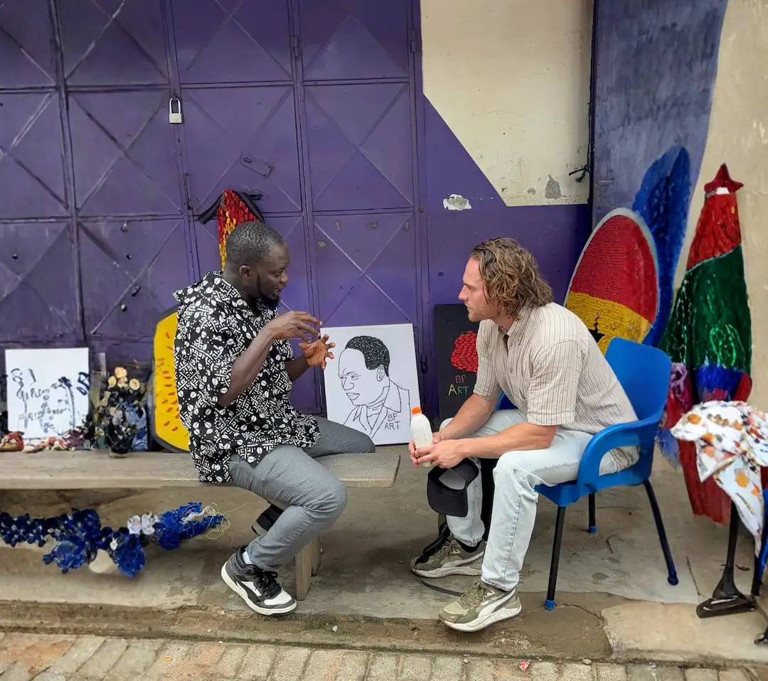 Twee mannen zitten te praten voor een paarse muur, met tussen hen in een kleine portrettekening van Martin Luther King Jr.