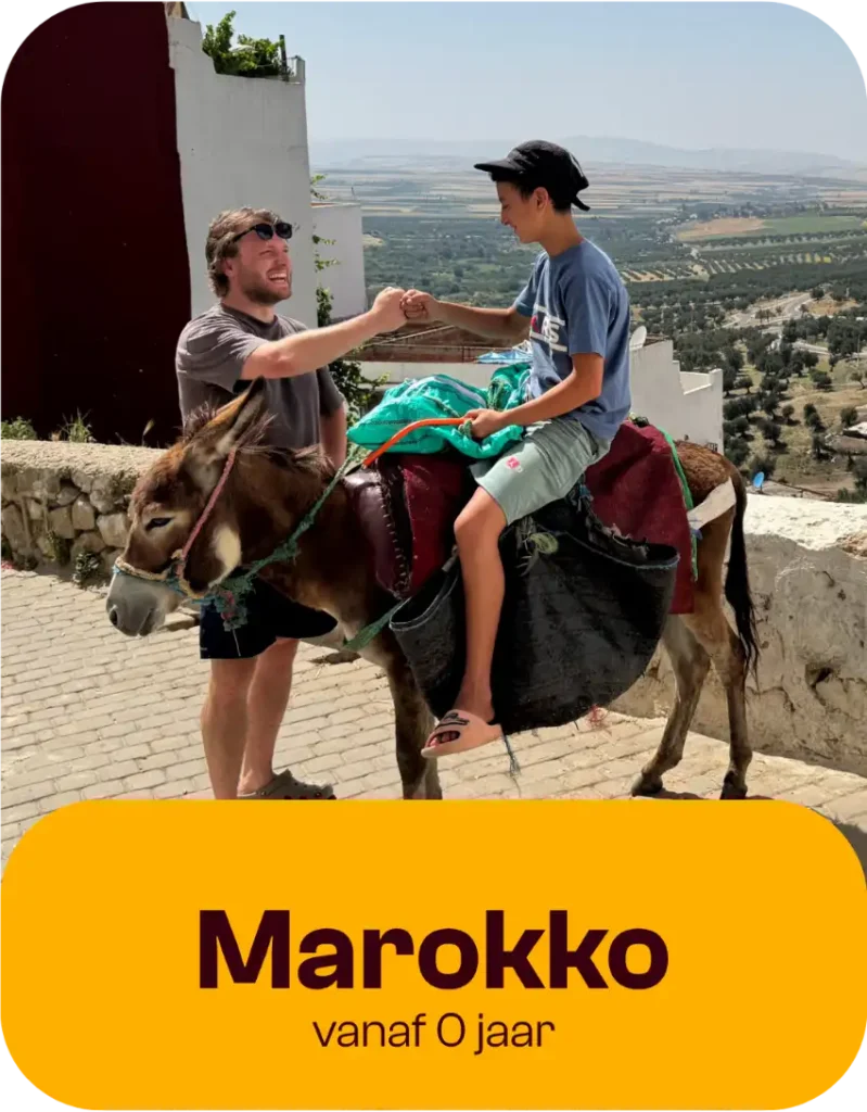 Een man en een jongen op een ezel geven elkaar glimlachend een fist bump, met op de achtergrond een schilderachtig landschap en een wit gebouw. De tekst luidt: „Marokko vanaf 0 jaar...“.