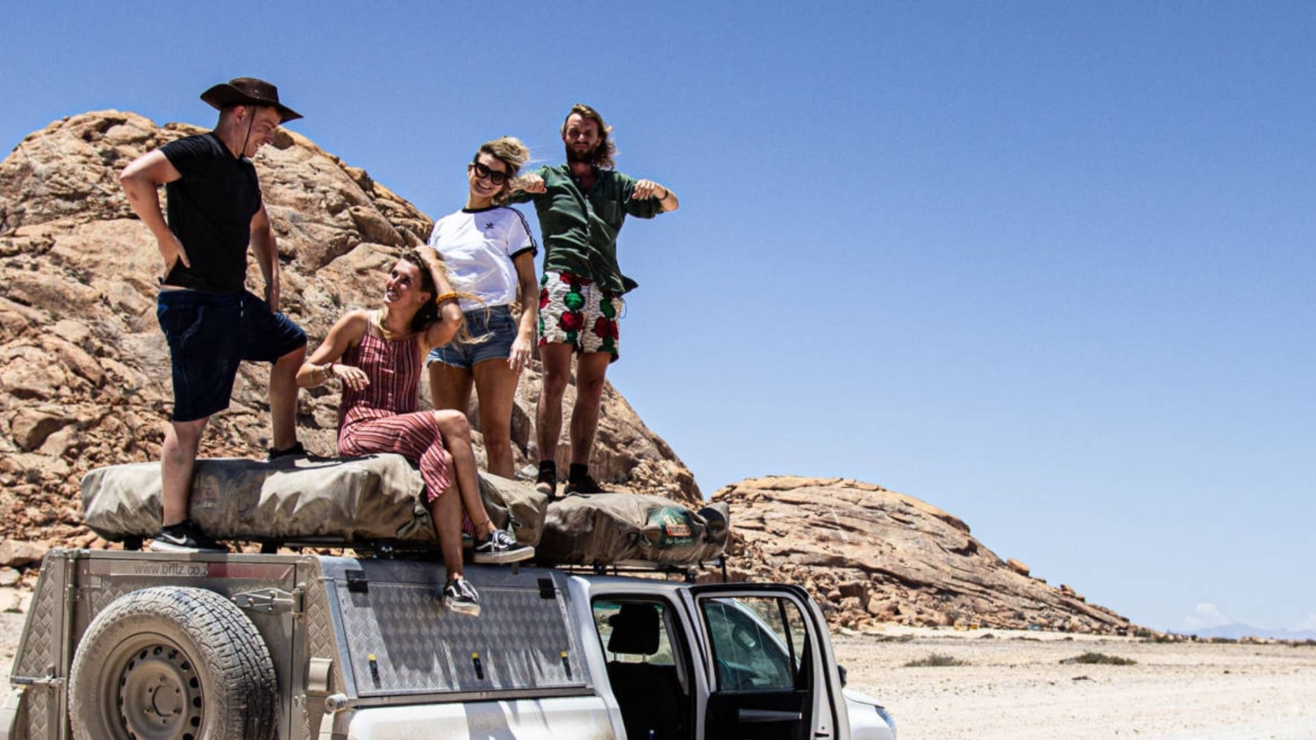 vier vrienden poseren lachend op daktent in rotsachtig woestijnlandschap namibië