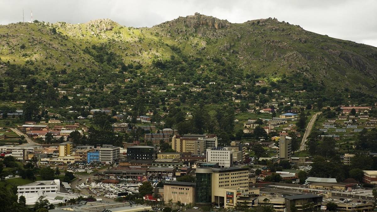 uitzicht op de stad mbabane in eswatini met moderne gebouwen aan de voet van een groene berghelling onder een bewolkte hemel