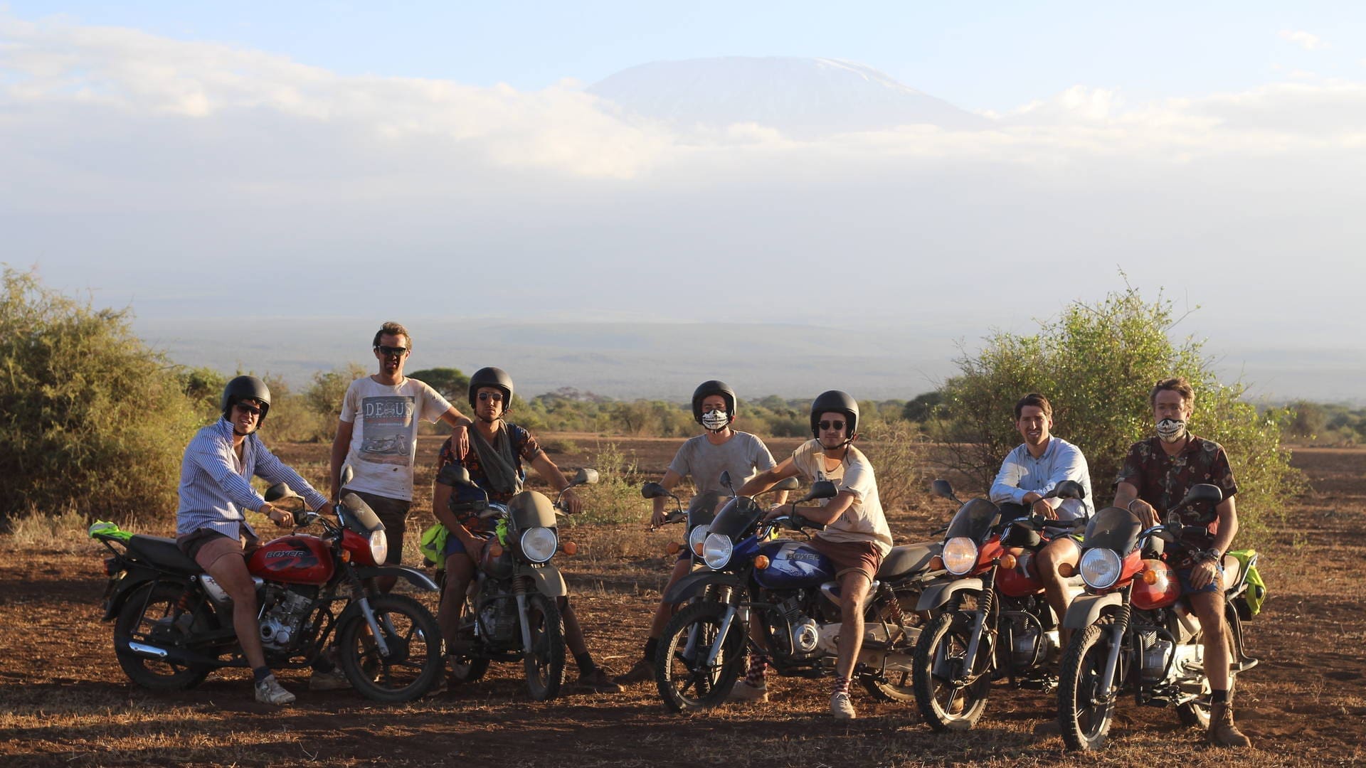 groep reizigers op motoren poseert voor een tocht door het droge savannelandschap van kenia met uitzicht op de besneeuwde top van de kilimanjaro