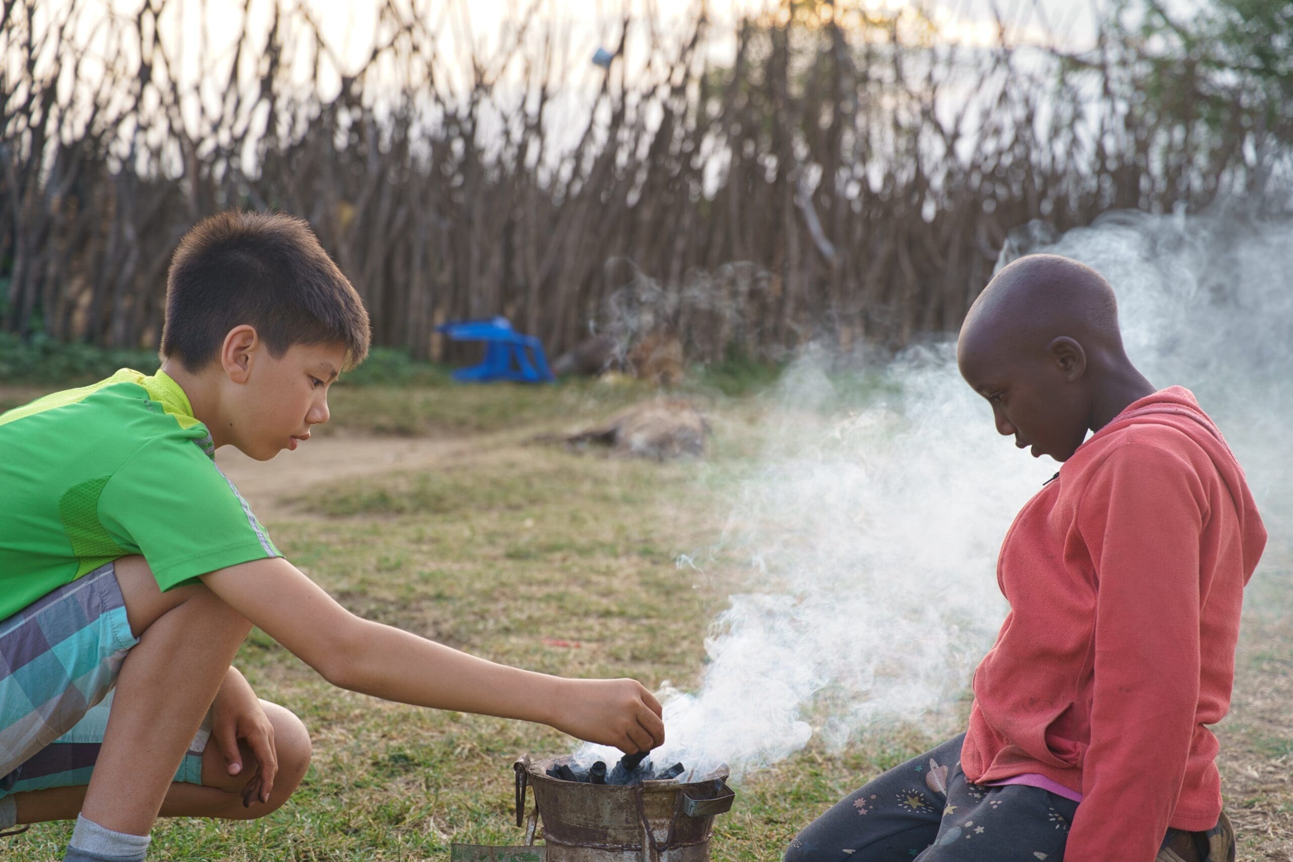 Twee kinderen zitten samen bij een rokend houtskoolvuurtje in een dorp in Kenia