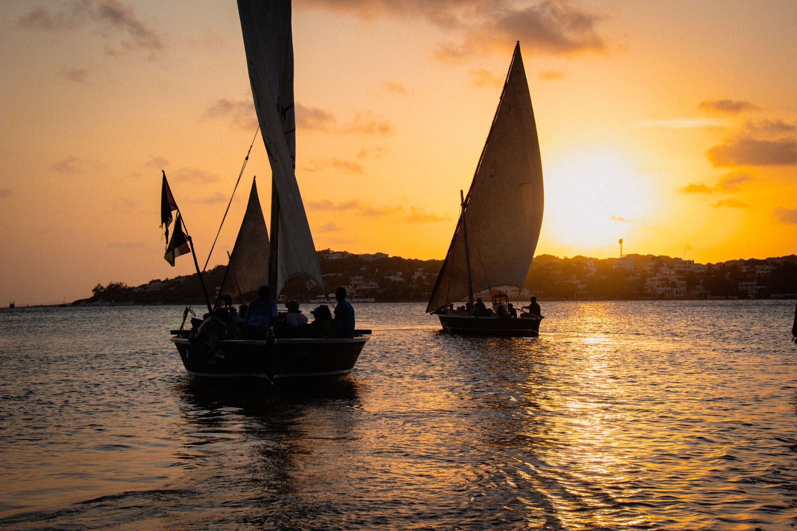 dhow boten met silhouetten van reizigers varen bij zonsondergang voor de kust van lamu kenia