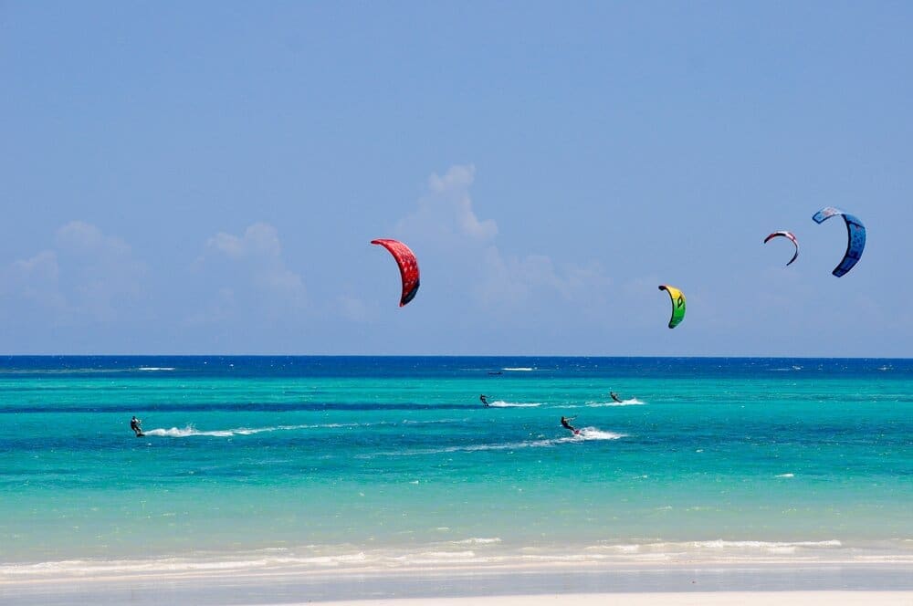 kleurrijke kitesurfers op helderblauw water bij een tropisch strand