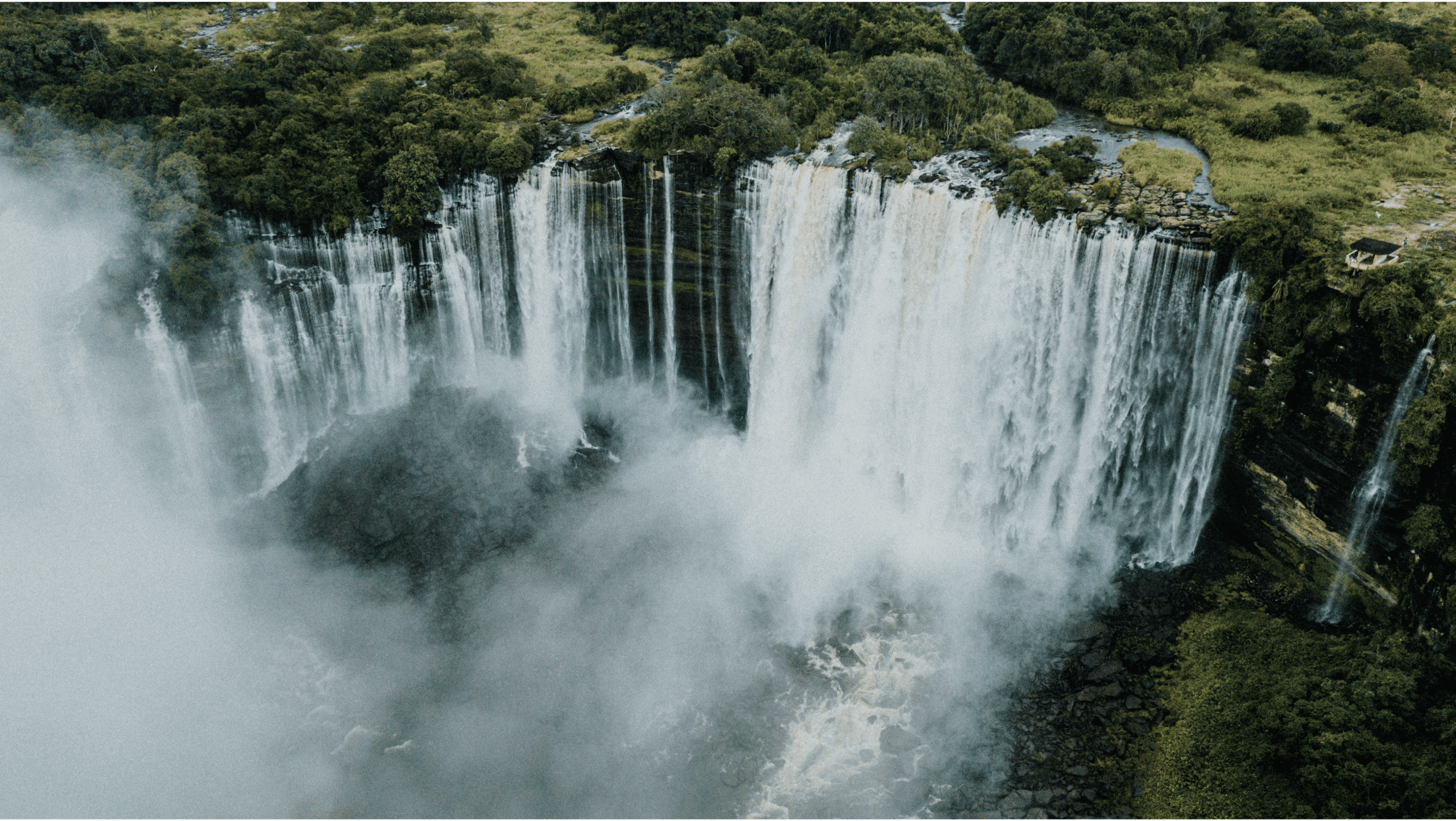 Luchtfoto van een brede, krachtige waterval die over een weelderige groene klif in Angola stort, met oprijzende mist en dichte bossen rondom het gebied - een onvergetelijke reiservaring in Afrika.