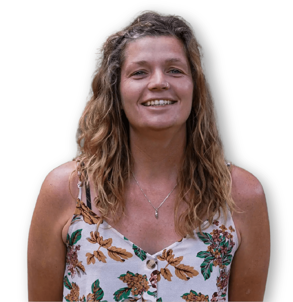 Een vrouw met golvend lichtbruin haar die een mouwloos topje met bloemmotief en een ketting draagt, glimlacht naar de camera tegen een effen witte achtergrond.