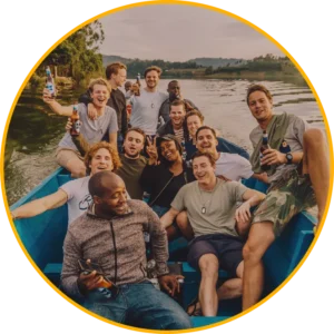 Een groep vrienden, met drankjes in de hand en glimlachend, zit samen op een boot op een meer omringd door groen. De scène wordt omlijst door een felgele cirkelvormige rand.